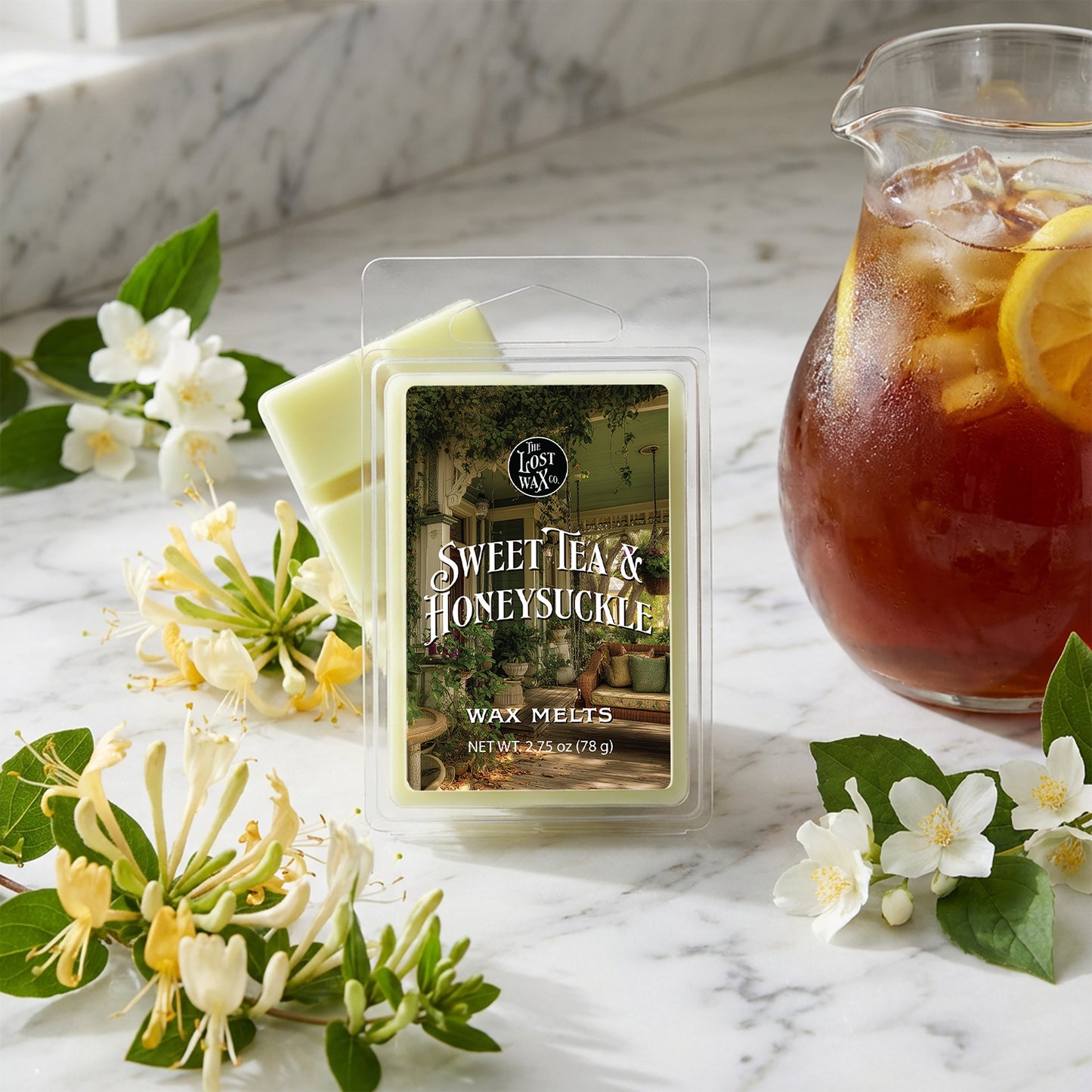 Packaged wax melts labeled 'Sweet Tea & Honeysuckle' with a pitcher of iced tea and flowers on a marble surface.