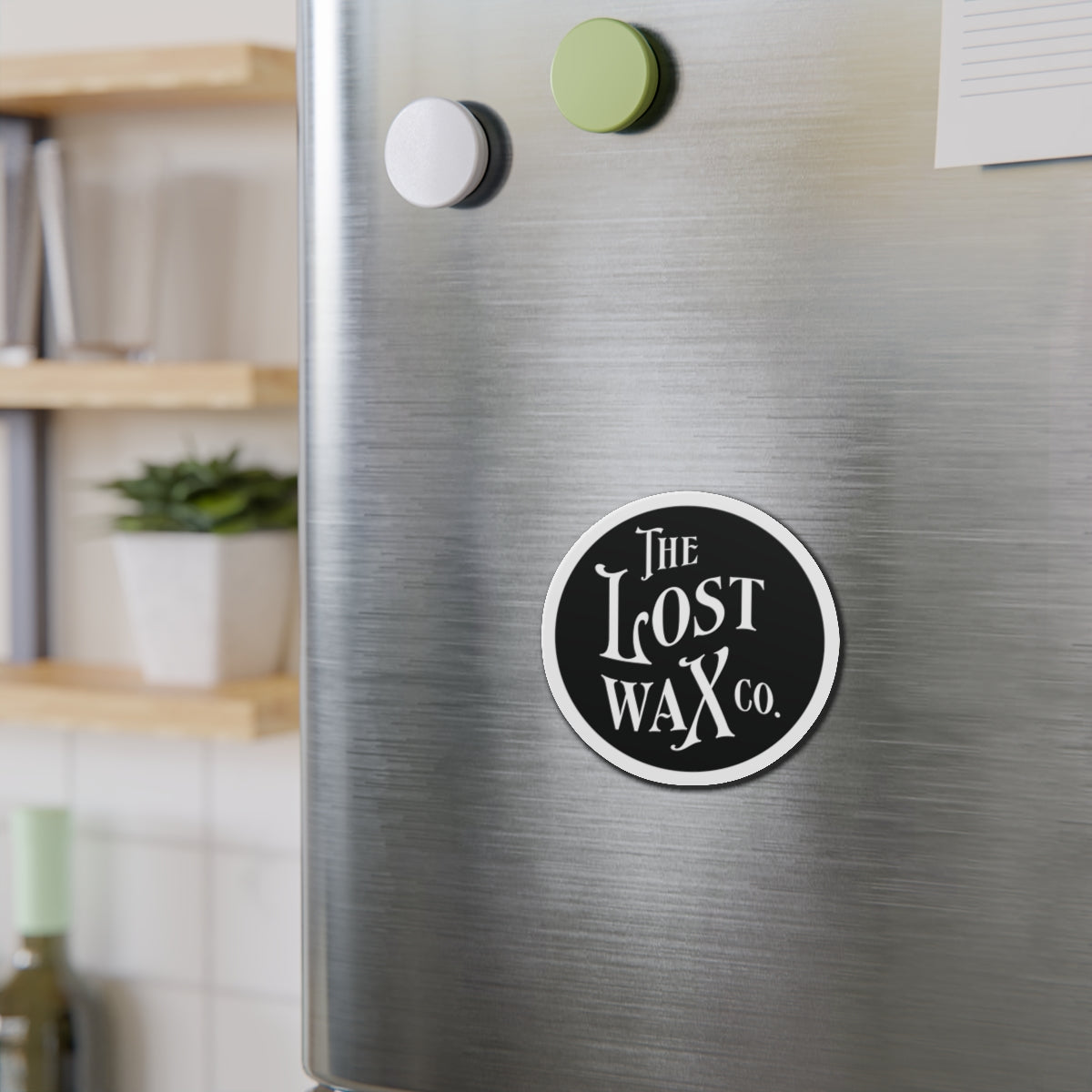 Round magnet with 'The Lost Wax Co.' logo on a metallic surface.