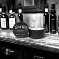 Candle and container labeled 'The Lost Wax Company' on a shelf with bottles in the background