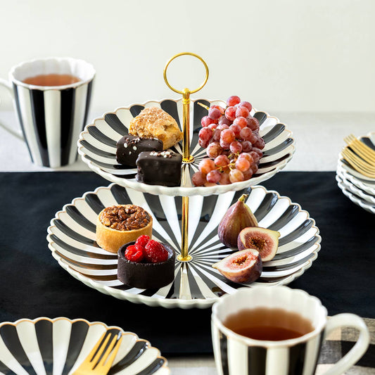 Three-tiered dessert stand with pastries, fruits, and tea cups on a table.