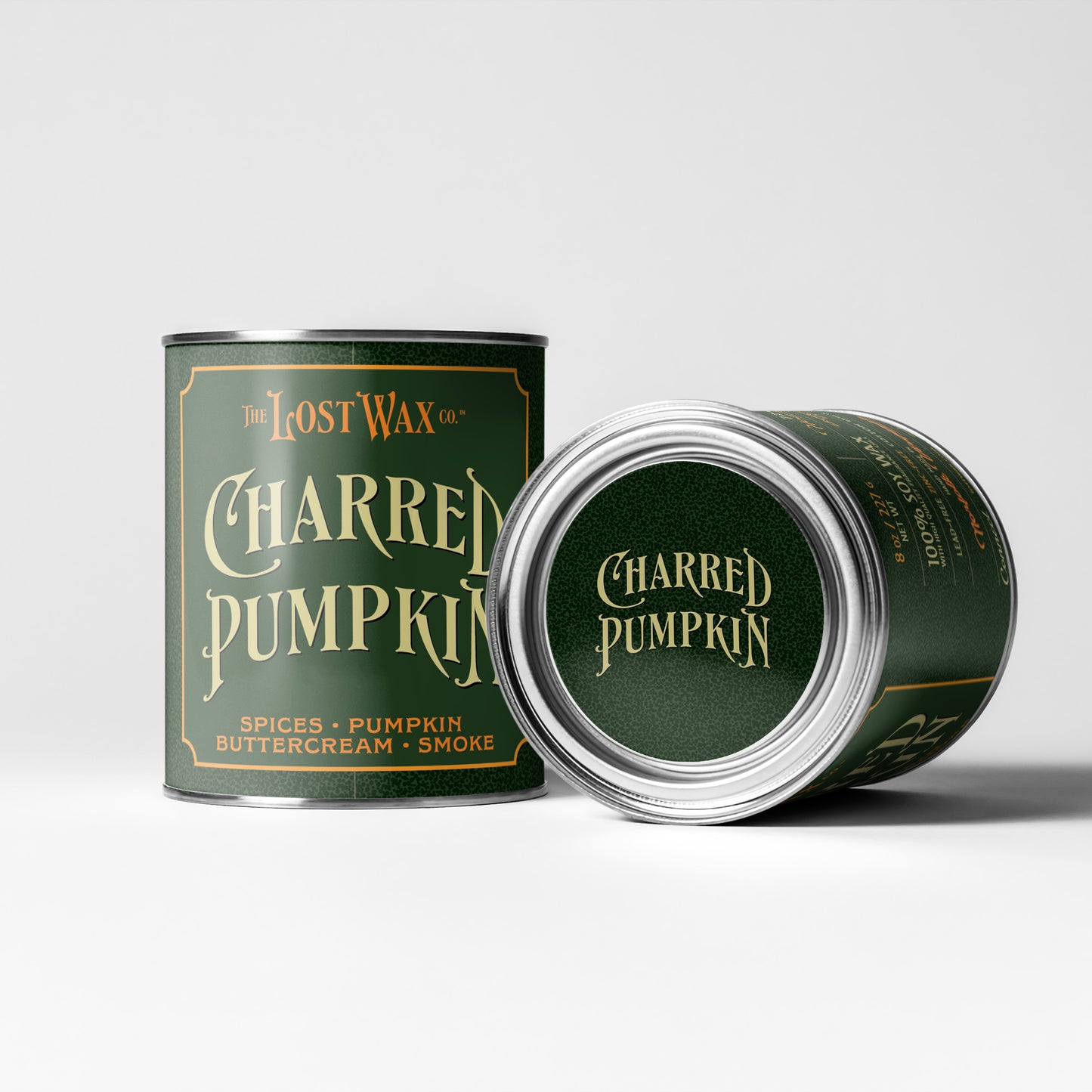 Two metal tins of The Lost Wax Co. Charred Pumpkin candles on a light gray studio background.