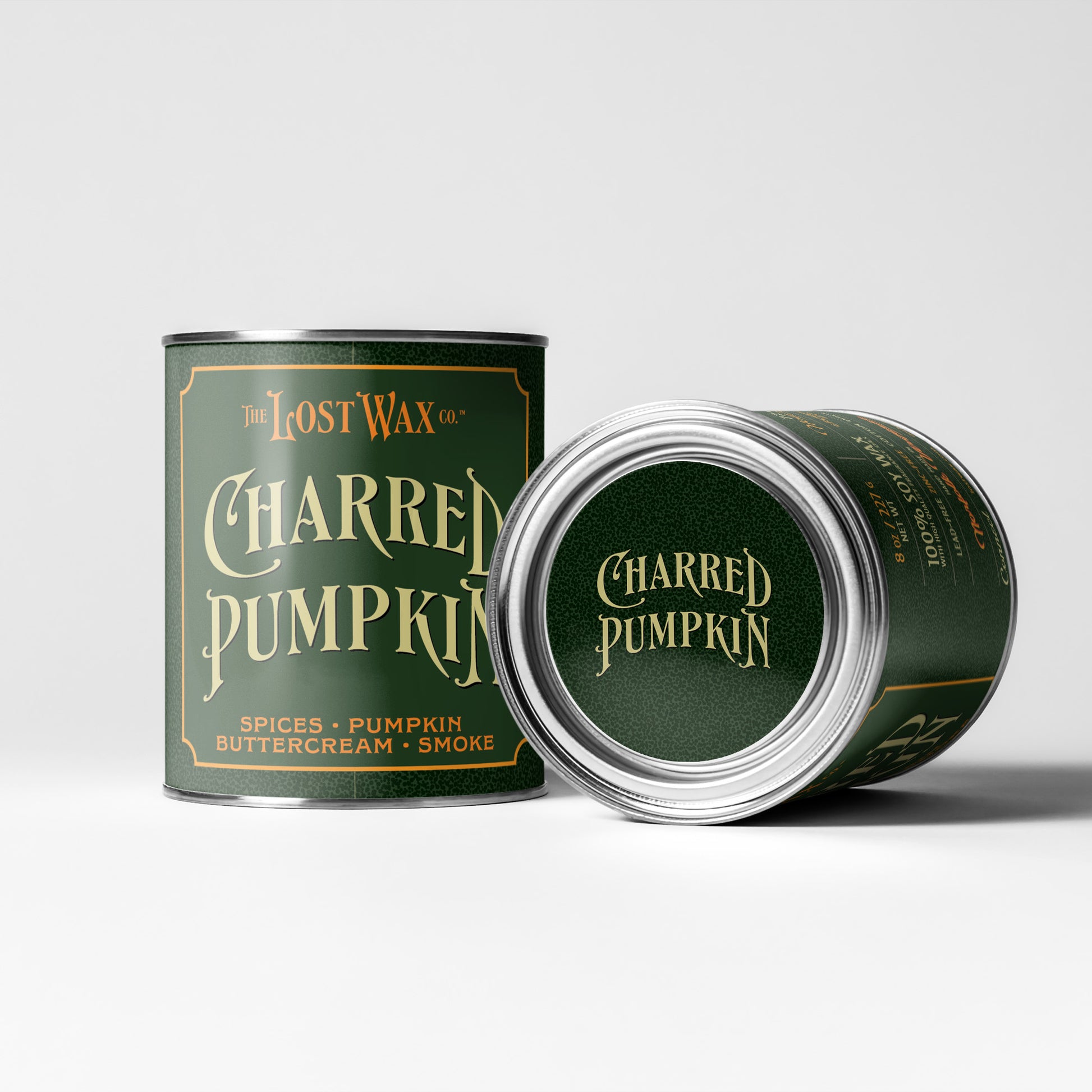 Two metal tins of The Lost Wax Co. Charred Pumpkin candles on a light gray studio background.