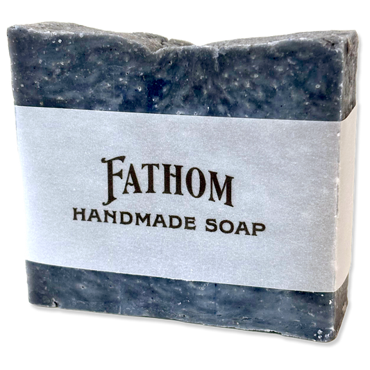 A rectangular bar of Fathom Handmade Soap with a textured dark gray and blue marbled finish, wrapped in a white paper band with black text.