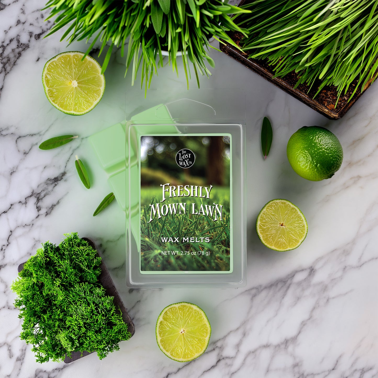 Wax melts packaging labeled 'Freshly Mown Lawn' surrounded by greenery and limes on a marble surface