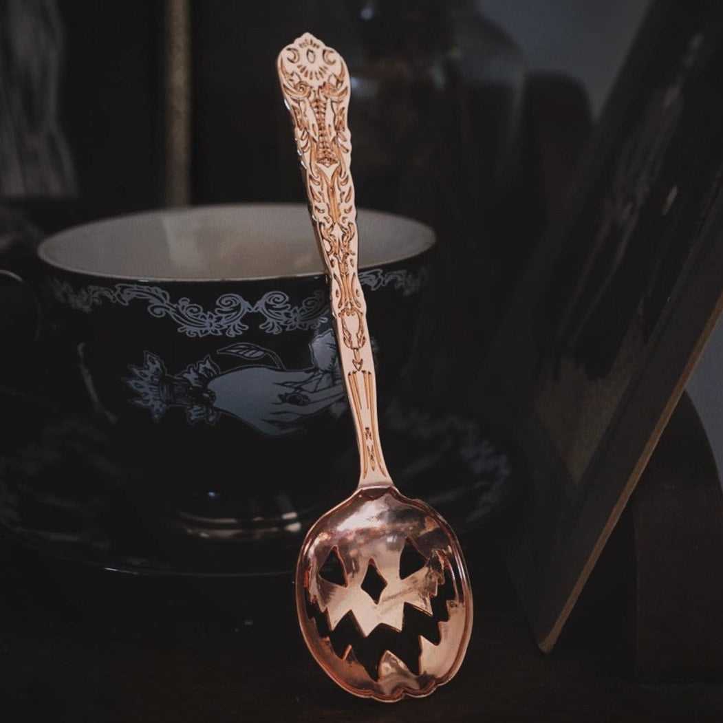 Decorative spoon with intricate patterns in front of a black mug with white design.