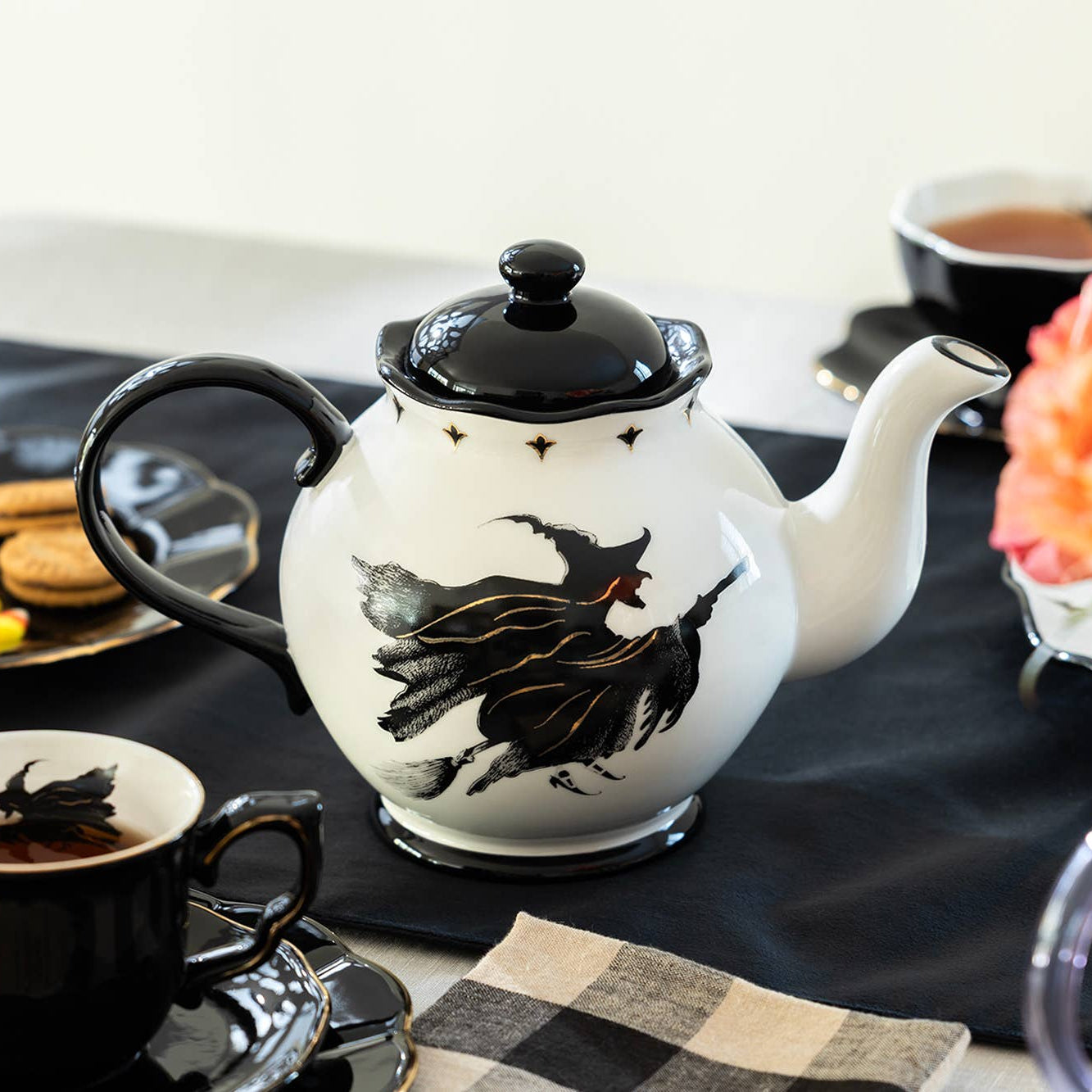 Teapot with witch design on a table with coffee and flowers