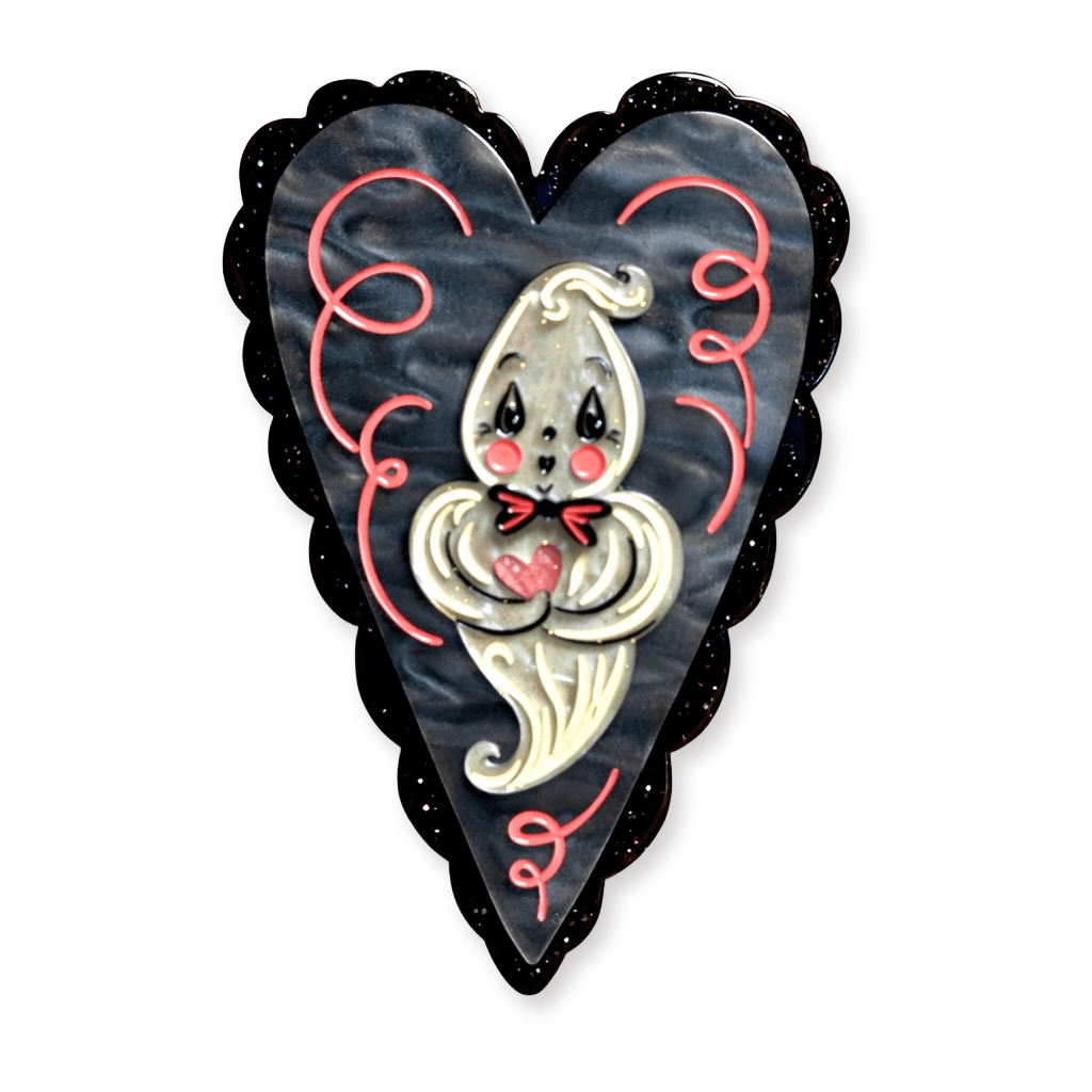 A heart-shaped brooch featuring a cute cartoon ghost with a red bow tie and pink heart, set against a dark marbled background with a black scalloped border.