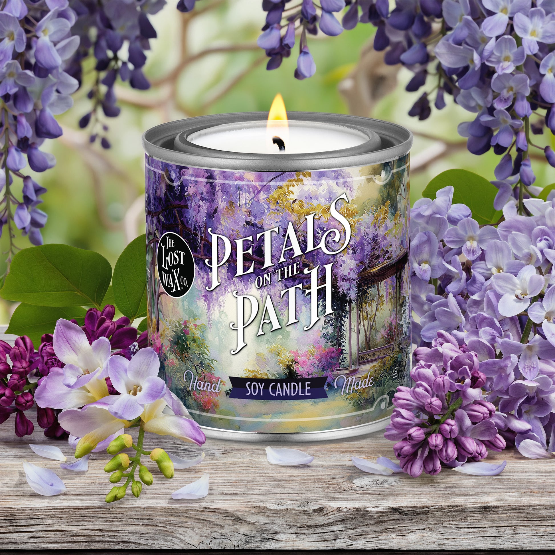 Candle labeled 'Petals on the Path' surrounded by purple flowers on a wooden surface
