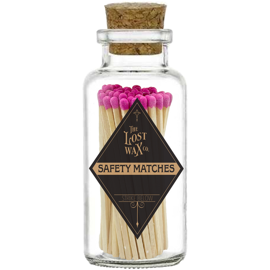 Glass jar with cork lid containing pink-tipped safety matches branded 'The Lost Wax Co'.