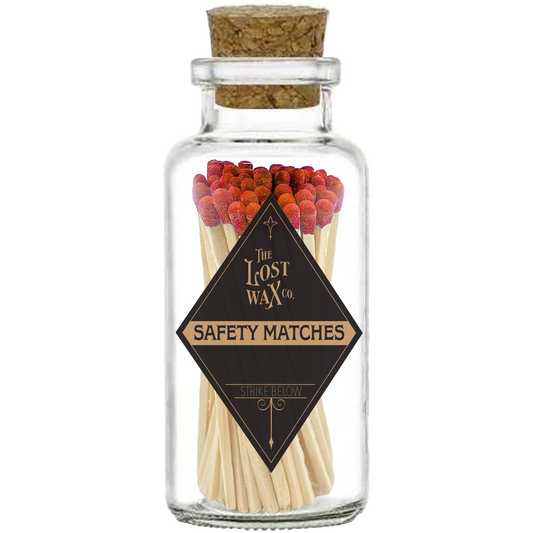 Glass jar with cork lid containing red safety matches branded 'The Lost Wax Co'.