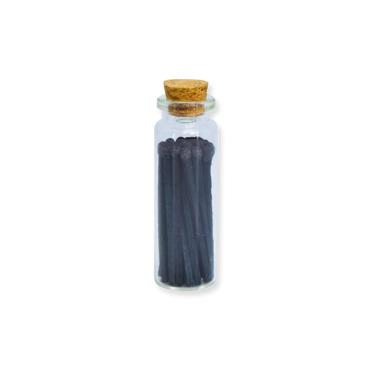 Small glass bottle with cork lid containing dark sticks on a white background