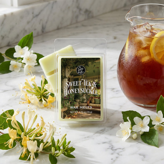 Packaged wax melts labeled 'Sweet Tea & Honeysuckle' with a pitcher of iced tea and flowers on a marble surface.